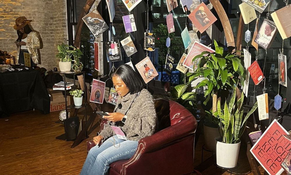 A person sitting in a chair and exploring the offerings at the Black Future Newsstand exhibit at AfroTech