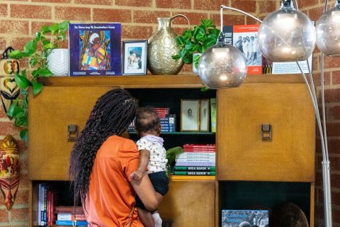 A woman holding a baby examines objects in the living room created for the Black Future Newsstand exhibit in Los Angeles.