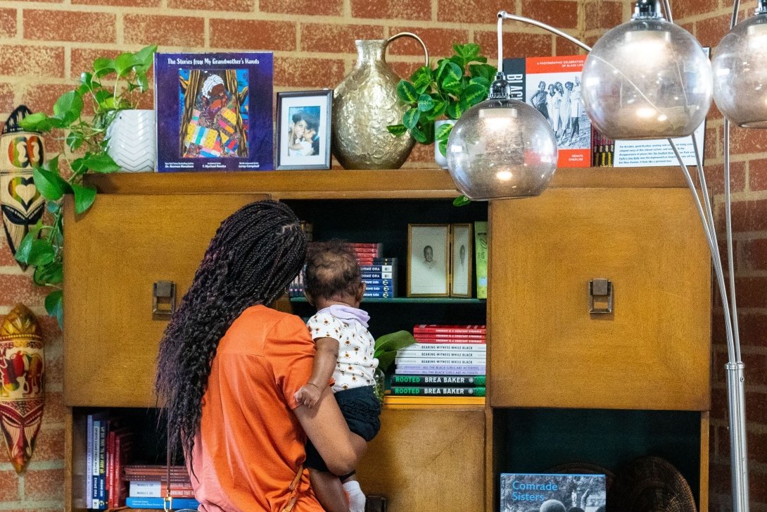 A woman holding a baby examines objects in the living room created for the Black Future Newsstand exhibit in Los Angeles.